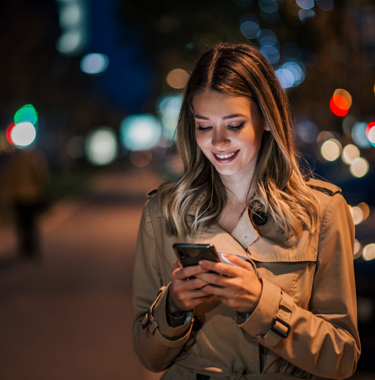 Portrait of a smiling young woman using smart phone at night.
